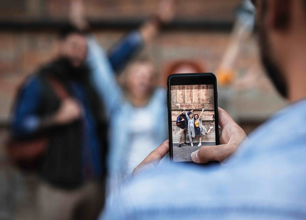 Group of tourists enjoying on vacation, young man photographing his friends with smart phone.