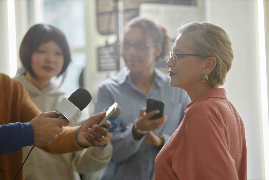 Middle Aged Caucasian Woman Giving Interview to Multiethnic Journalists Indoors